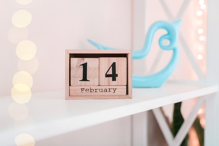 February 14 date on wooden label calendar place on white shelf with blue bird and lights. Valentine's day concept.の写真素材