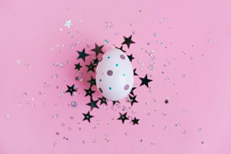 Egg decorated with dots on pink background with star glitter confetti, Easter concept. Top view.の写真素材