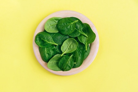 Green fresh vegetarian salad leaves on wooden plate on yellow background. Top view. Healthy and zero waste life concept.の写真素材