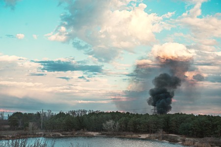 Forest fire near the lake and stunning sky with light and dark clouds background. Landscape.の写真素材