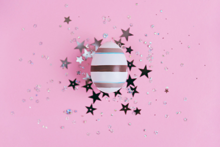 Egg decorated with stripes on pink background with star glitter confetti, Easter concept. Top view.の写真素材