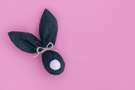 Easter bunny gift egg wrapped in black craft paper on pink background. Top view, copy space.