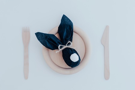 Easter bunny gift egg wrapped in black craft paper on wooden plate with fork and knife. Top view.の写真素材