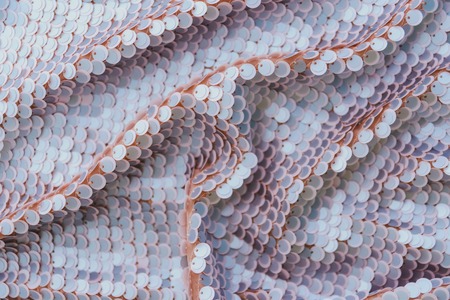 Pale pink shiny fabric with sequins, abstract background. Close-up.