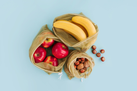Reusable bags with fruits and nuts on blue background. Zero waste and plastic free shopping concept. Top view.の写真素材