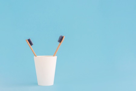 Two wooden toothbrushes in cup on blue background.の写真素材