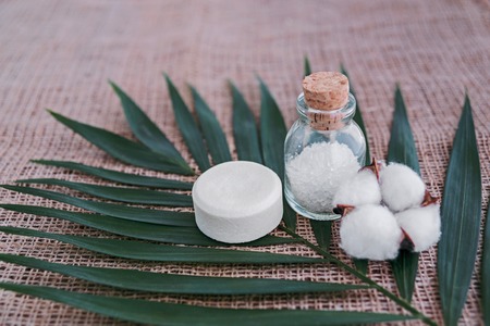 Soap, sea salt in glass bottle and cotton flower on palm leaf background. Spa concept.