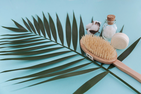 Soap, sea salt in glass bottle, natural brush and cotton flower on palm leaf blue background. Top view.の写真素材