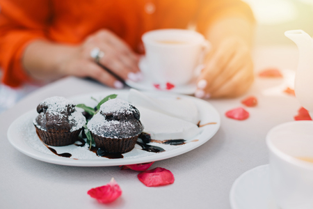 Tea cups and womans hands holding one cup on table with rose petals, top view.の写真素材