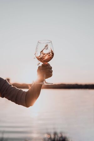 Glass of rose wine in woman's hand against the sunset sky. Cropped.の写真素材