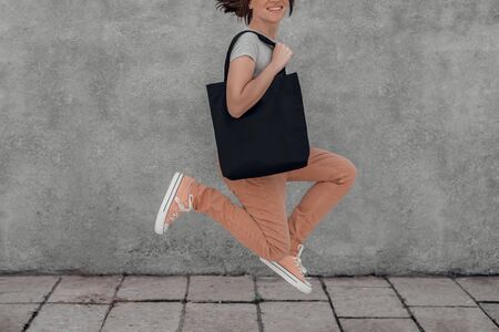 Young woman is jumping with black cotton bag in her hands. Mock-up. Cropped.の写真素材