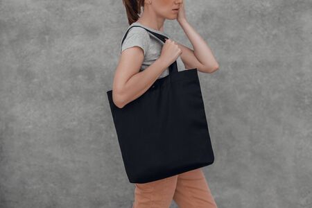 Young woman with black cotton bag in her hands on grey background. Cropped.