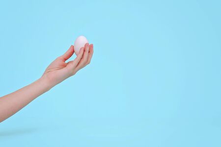 Woman's hands with white egg on pastel blue background. Easter concept. Copy space.の写真素材