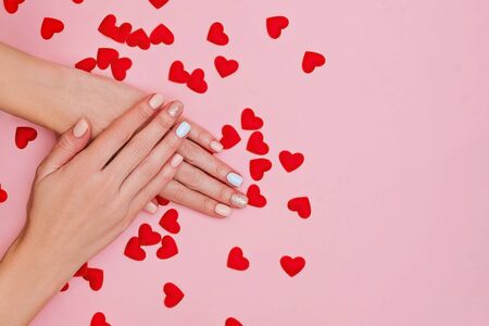 Woman's hands with pastel manicure on pink background with red hearts. Valentine's day concept. Place for text.の写真素材
