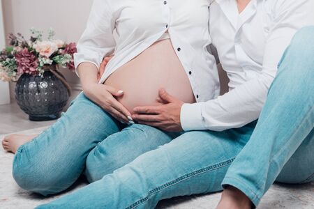 Pregnant woman and her husband are holding hands on belly. Cropped.の写真素材