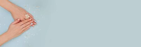 Woman's hands with pastel manicure on blue background with fresh white flowers. Banner with place for text. Copy space.の写真素材