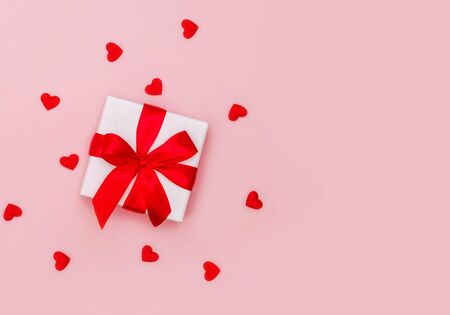 Gift box with red ribbon on pale pink background with red hearts. Festive concept. Place for text.の写真素材