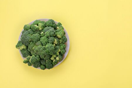 Fresh green broccoli on plate on yellow background. Top view. Copy space.の写真素材
