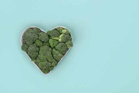 Heart shaped fresh green broccoli on plate on green background. Top view.の写真素材