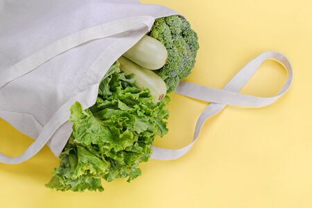 Reusable bag with green salad, broccoli and zucchini on yellow background. Zero waste and plastic free shopping concept. Top view.の写真素材