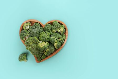 Heart shaped fresh green broccoli on wooden plate isolated on white. Top view.の写真素材