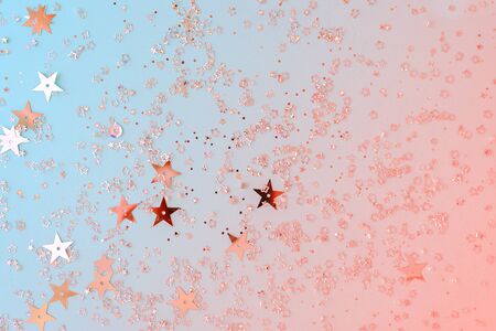 Delicate glitter star confetti on coral and blue background. Creative and moody color of the picture. Top view.の写真素材