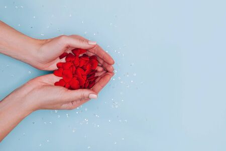 Woman's hands full of small red hearts on blue background. Love, care, affection, the St. Valentine's day concept. Place for text.の写真素材