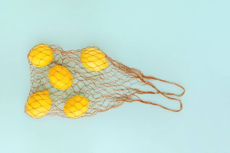 Reusable bag with lemons on blue background. Zero waste and plastic free shopping concept.