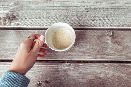 Woman's hand in blue sweater holding empty cup of coffee on the grey wooden table. Top view.の写真素材