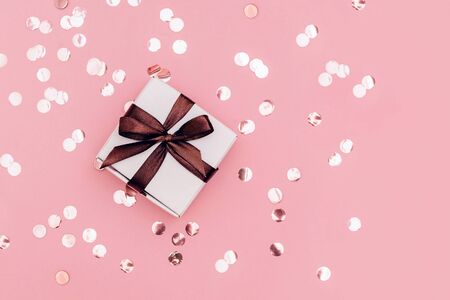 Cute gift box with brown ribbon on pale pink background with glitters. Festive concept. Place for text.の写真素材