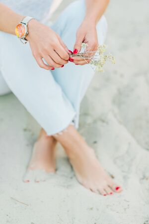 Woman feet with red pedicure in the beach sand. Cropped.