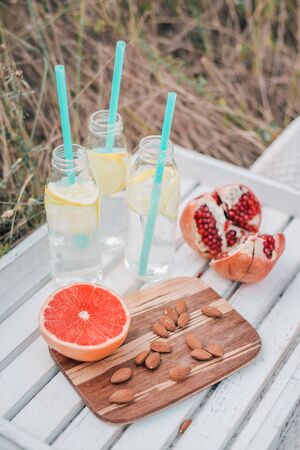 Picnic set with grapefruit, pomegranate, almond nuts and lemonade in glass bottles on white wooden tray.の写真素材