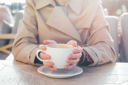 Big coffee white cup in woman's hands with pastel manicure while sitting in cafe. Cropped.の写真素材