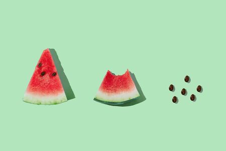 Slice of ripe watermelon and seeds on mint green background with copy space. Process of eating watermelon from whole slice to seeds. Flat lay, top view.の写真素材