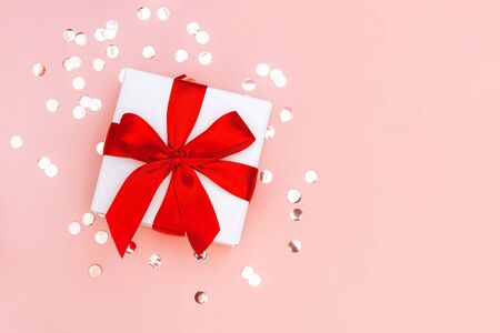 Gift box with red ribbon on pale pink background with golden confetti. Festive concept. Place for text.の写真素材