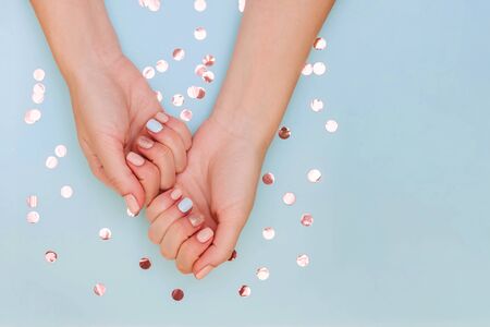 Woman's hands with pastel manicure on blue background with copy space and golden confetti. Top view.の写真素材