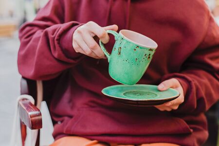 Big mint green tea cup in woman's hands with pastel manicure while sitting in cafe. Cropped.の写真素材
