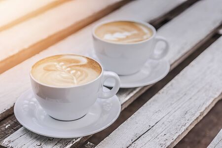 Two white big cups of coffee with art on white wooden table with copy space. Close up.の写真素材