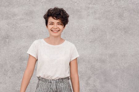 Charming young dark-haired woman with curly hairstyle smiling and posing. Human emotions and feelings.の写真素材