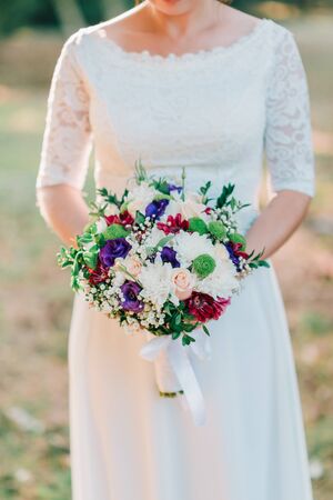 Hands of bride with wedding beautiful bouquet of white, purple and pink flowers.の写真素材