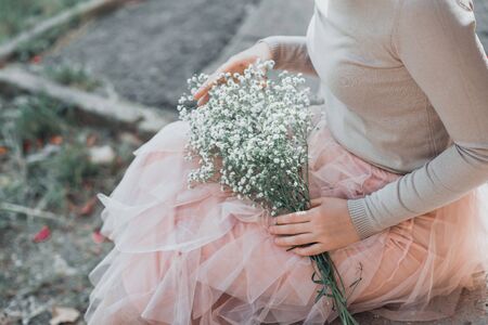 Woman in pink lace skirt with white flowers bouquet in her hands is sitting on stairs. Cropped.の写真素材