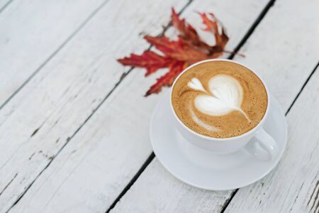 White big cup of coffee with art on white wooden table and autumn leaves with copy space. Top view.の写真素材