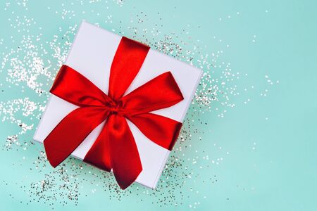 Gift box with red bow on green mint background with delicate golden sparkles. Top view.の写真素材