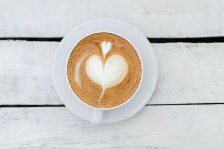 White big cup of coffee with shaped heart art on white wooden table with copy space. Top view.の写真素材