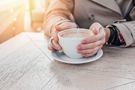 Big coffee white cup in woman's hands with pastel manicure while sitting in cafe. Cropped, copy space.の写真素材