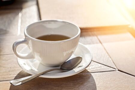 White big cup of black tea on wooden table in sunset light with copy space. Top view.の写真素材