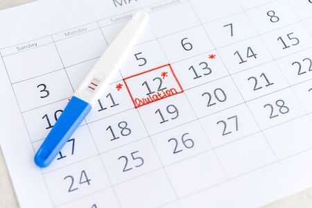 Positive pregnancy test with circling date in calendar. Planning of pregnancy, trying to have baby. Top view.の写真素材