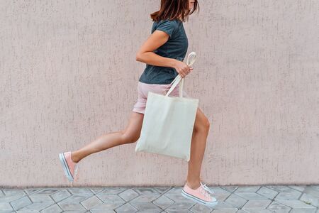 Woman in pink shorts and sneakers is jumping with white cotton bag in her hands.の写真素材