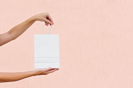 Woman hands with white paper shopping bag isolated on white on pink background. Mockup, copy space, shopping concept. Cropped.の写真素材