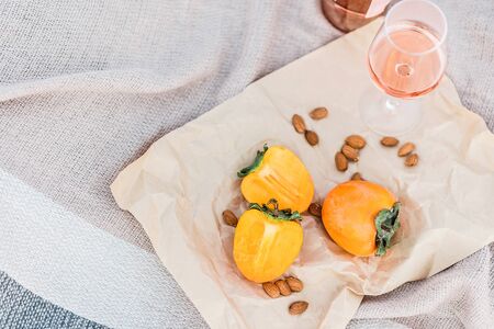 Picnic on the beach with persimmons, almond and bottle of rose wine on beige blanket. Lifestyle view.の写真素材